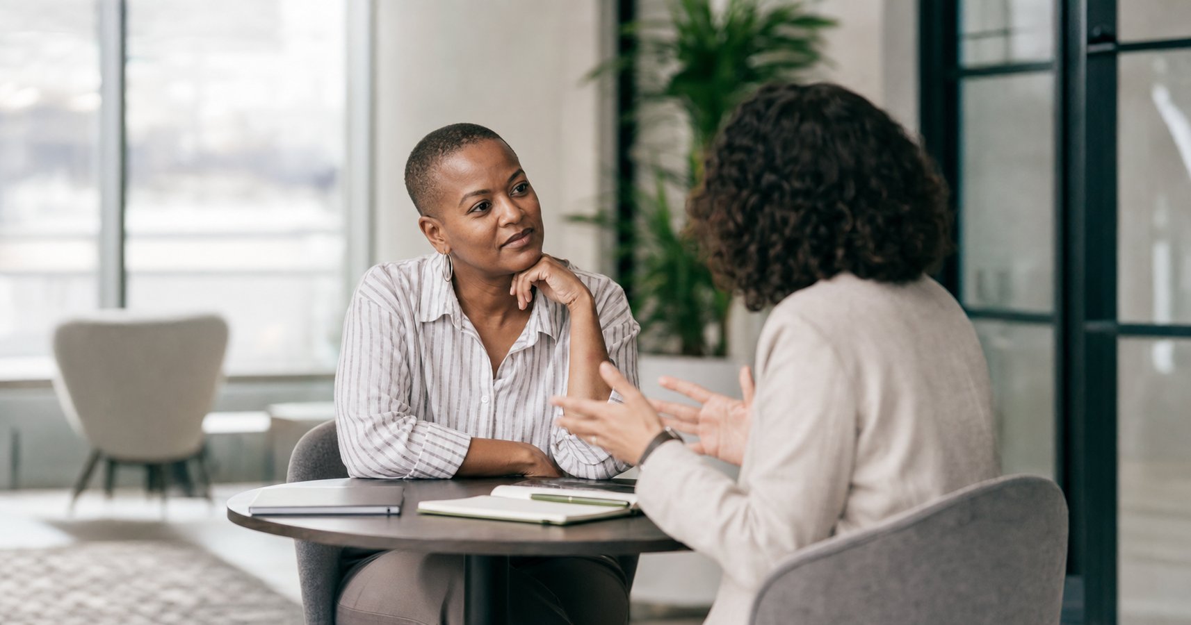 Two professionals seated in a modern office, engaged in a thoughtful coaching conversation at a small table with soft natural light.