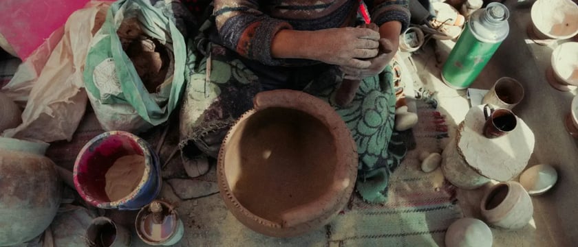 Overhead view of a potter working with clay, surrounded by bowls, pots and materials.