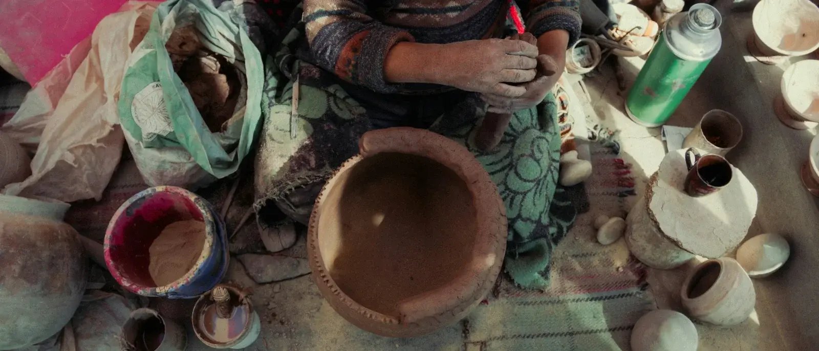 Overhead view of a potter working with clay, surrounded by bowls, pots and materials.