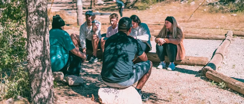 A group sitting in a circle and talking in a woodland clearing.