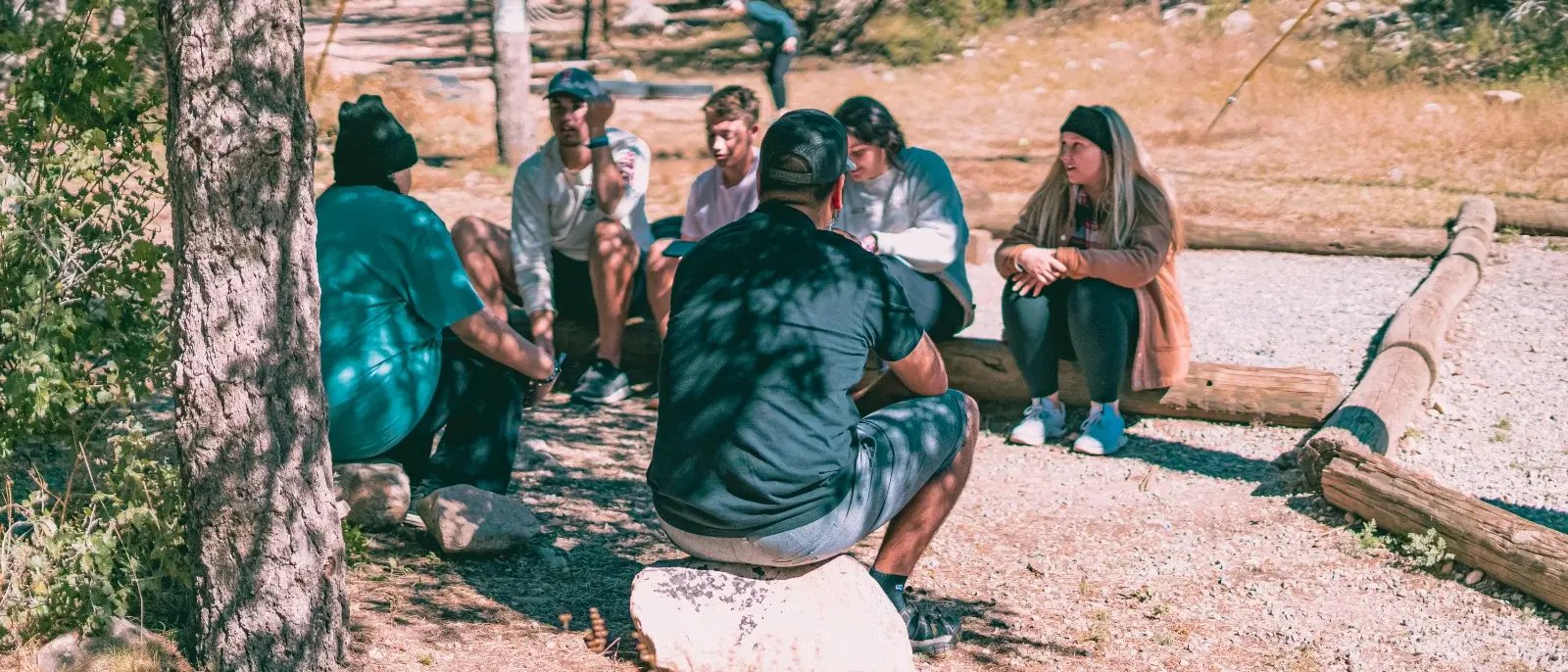 A group sitting in a circle and talking in a woodland clearing.