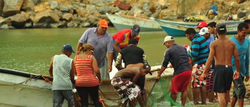 people gathering a fishing net beside a small boat in shallow water