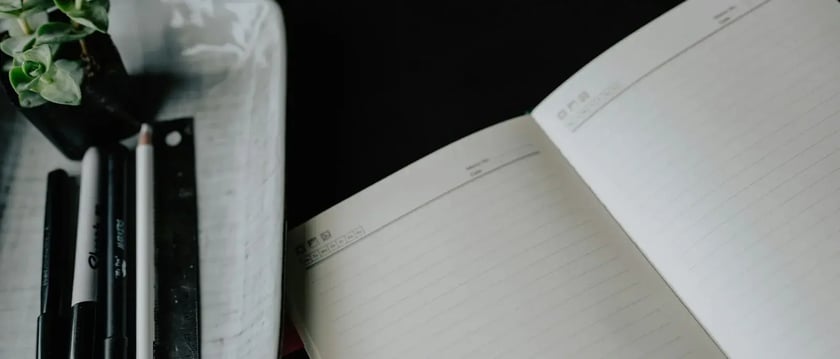 An open lined notebook sits beside neatly arranged pens and a ruler.