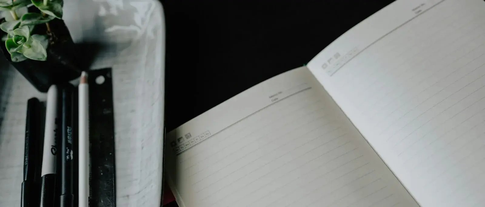 An open lined notebook sits beside neatly arranged pens and a ruler.