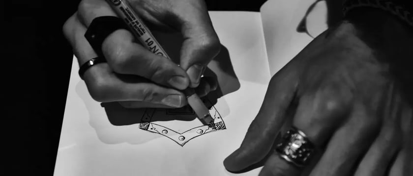Black-and-white close-up of hands drawing a geometric design in a sketchbook.