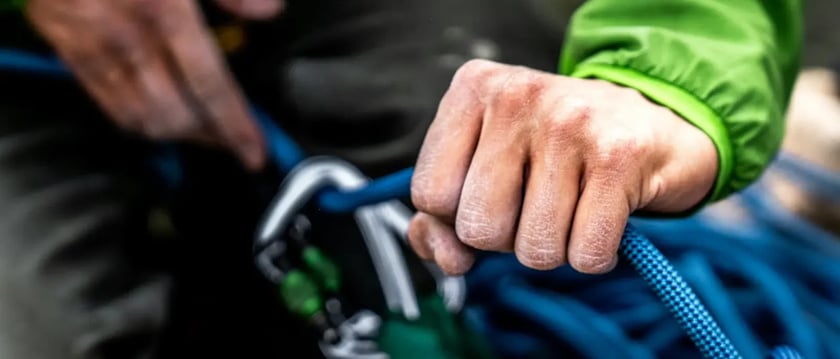 Close-up of a climber’s hands holding blue rope beside a carabiner.