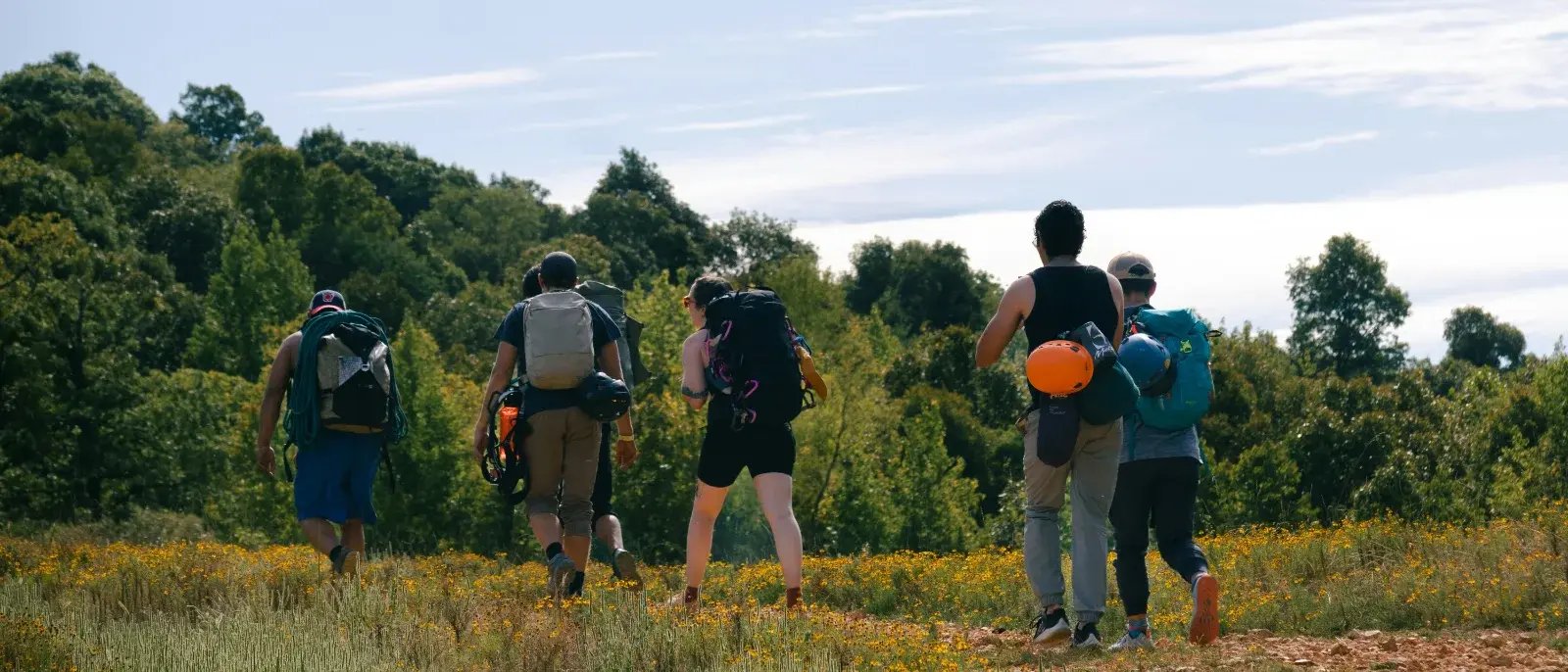 five hikers carrying backpacks across a grassy hillside