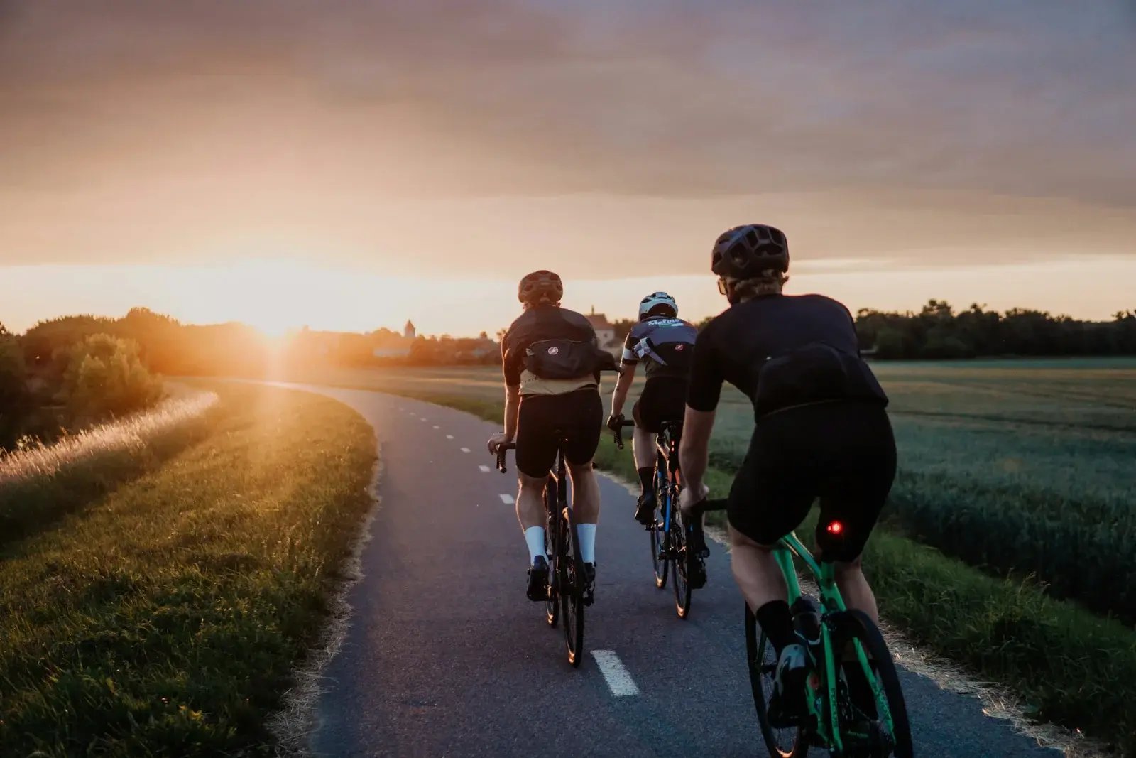 Three cyclists riding along a winding country road at sunset.